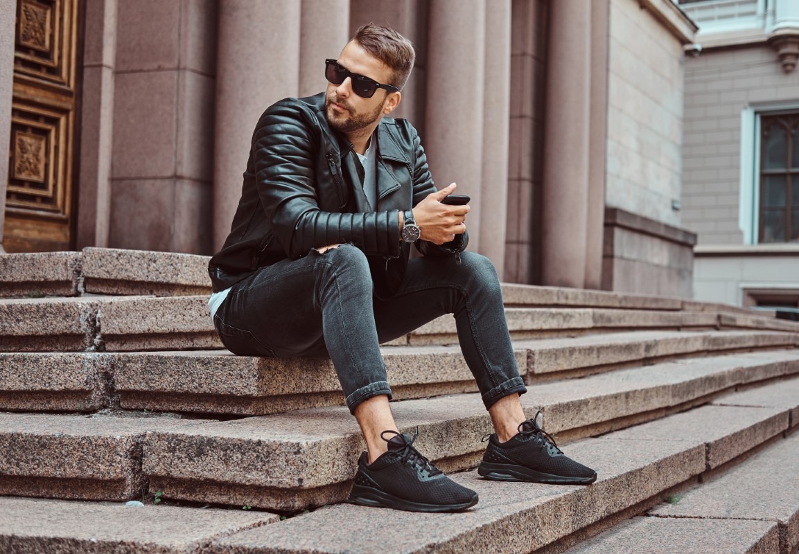Fashionable guy dressed in a black jacket and jeans sitting on steps against an old building in Europe. Babymoon, poslední dovolenou před porodem, si užijte sama i ve dvou.